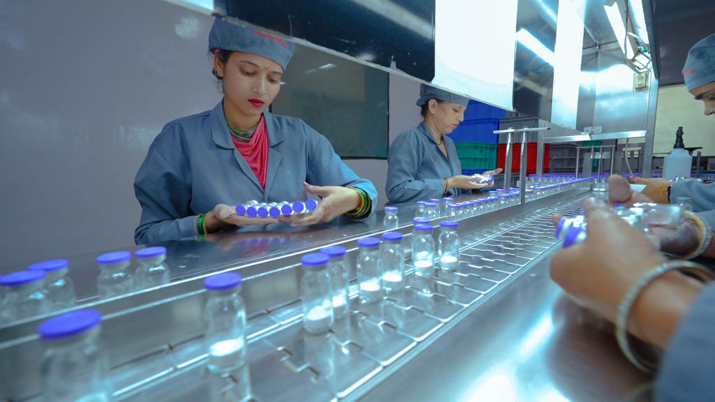 Pharmaceutical workers inspecting and assembling vials on clean conveyor